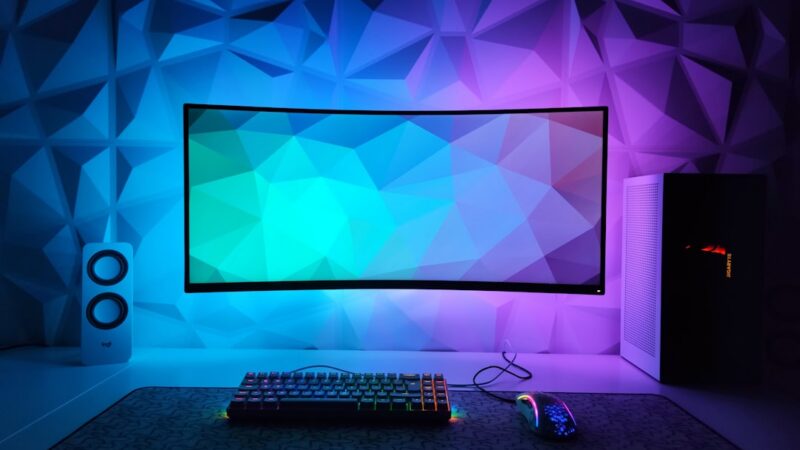 Computador de escritorio para juegos con teclado retroiluminado y monitor encendido, en un escritorio de casa
