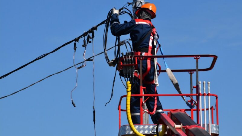 Trabajador realizando labores de mantenimiento en un poste de energía eléctrica, imagen de referencia