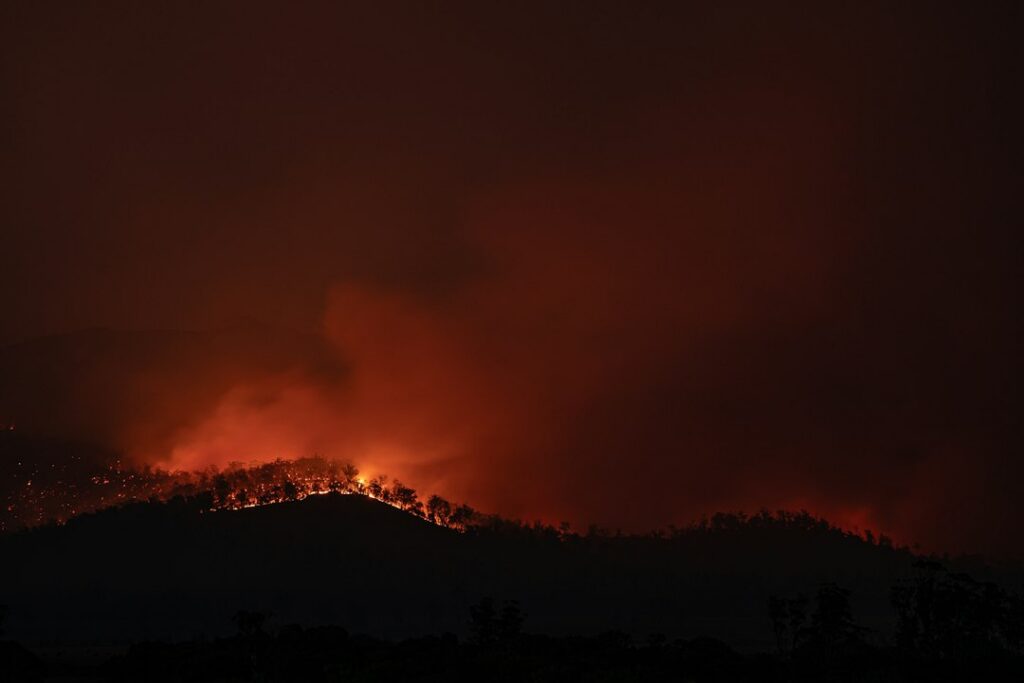 Bomberos trabajan en la extinción de un incendio forestal en una zona montañosa con vegetación y cultivos cercanos