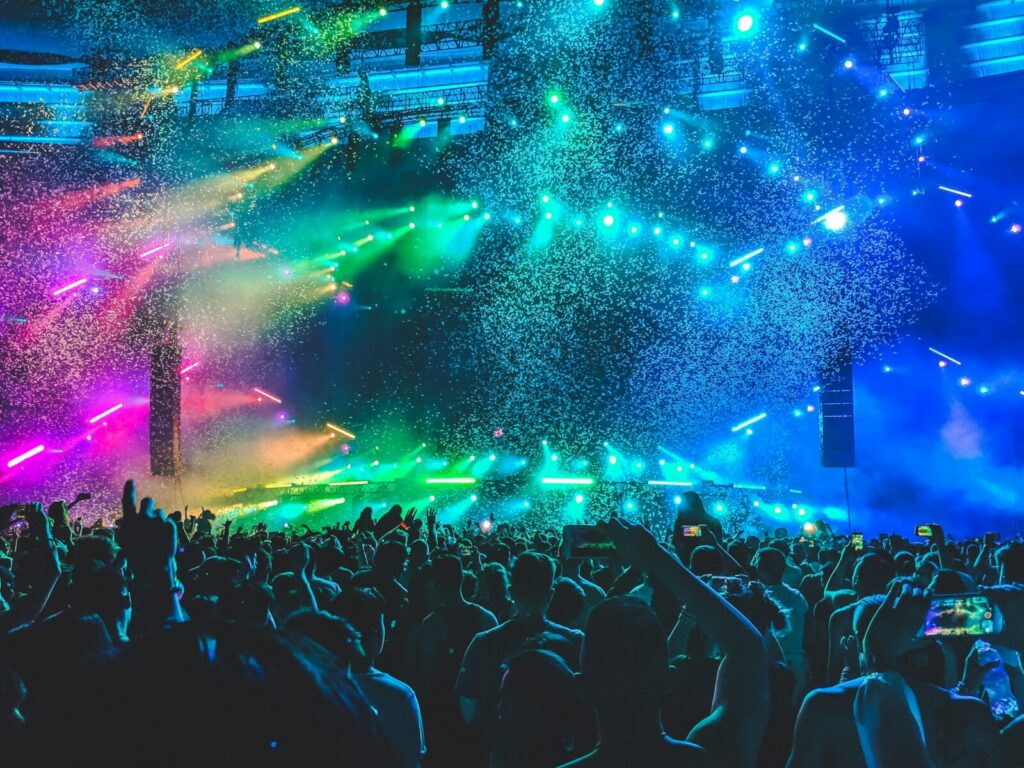 Asistentes en un festival de música al aire libre, con el escenario iluminado durante un concierto masivo