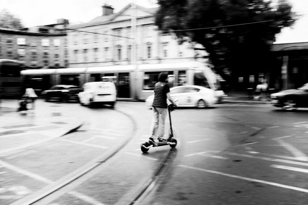 Persona circulando en patineta eléctrica por una avenida urbana con varias carriles