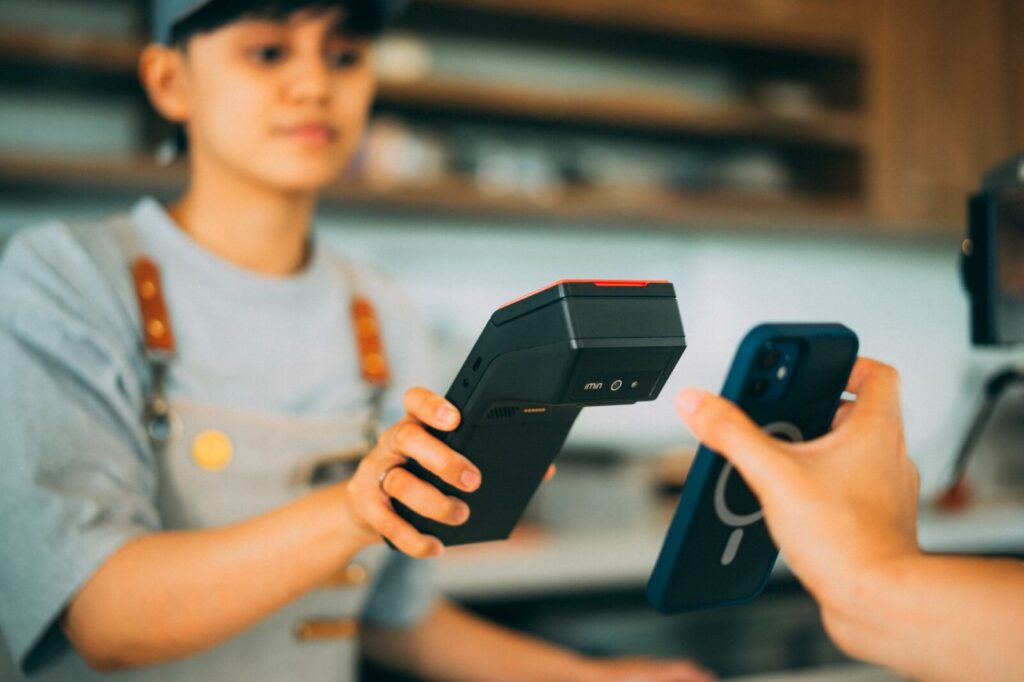Persona realiza un pago sin contacto acercando una tarjeta a un iPhone en un comercio