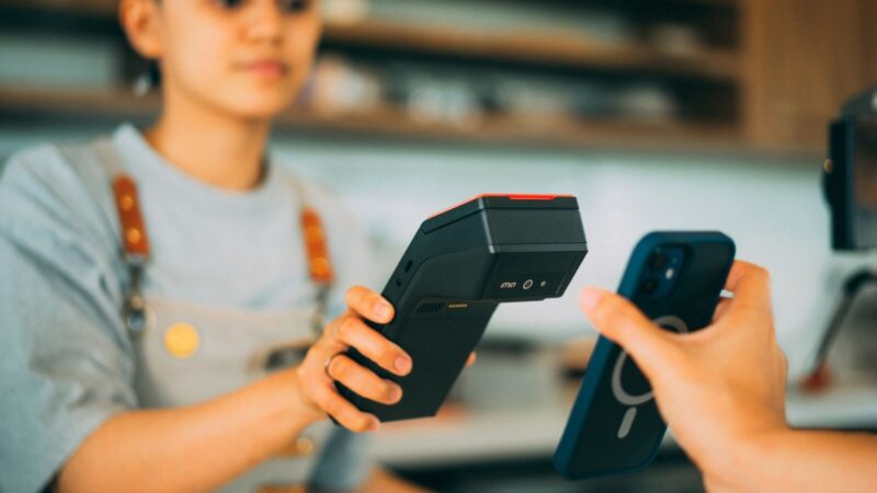 Persona realiza un pago sin contacto acercando una tarjeta a un iPhone en un comercio