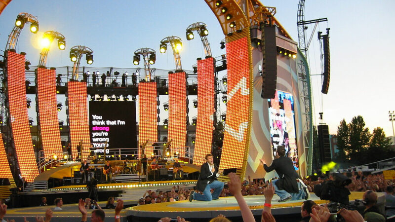 El cantante británico Robbie Williams durante una presentación en vivo, con luces de escenario y público asistente