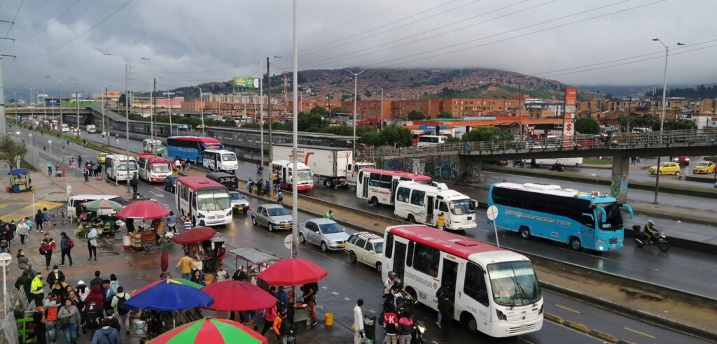 Vehículos circulando lentamente por una vía urbana durante una jornada de lluvia y congestión
