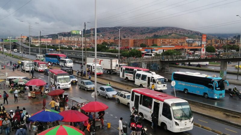 Vehículos circulando lentamente por una vía urbana durante una jornada de lluvia y congestión