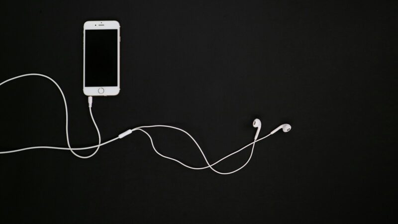 Celular con una aplicación de música abierta junto a audífonos, representando la reproducción de canciones sin conexión