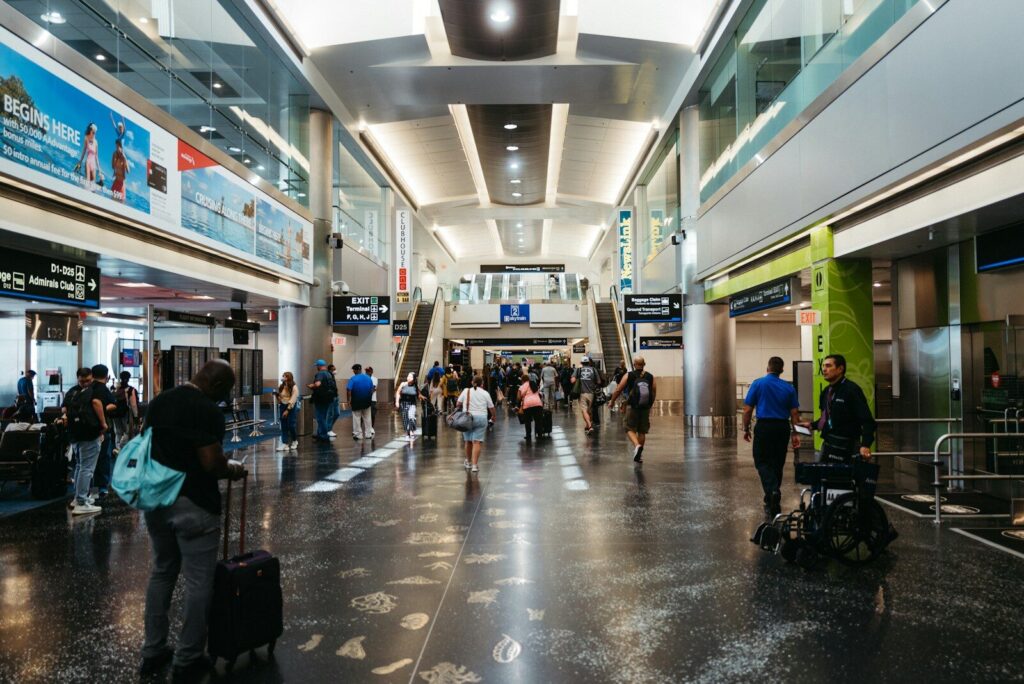 Pasajeros en una terminal aeroportuaria junto a paneles de información sobre sus vuelos.