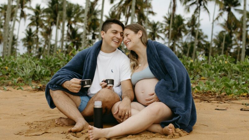 Pareja anunciando un embarazo junto a una ecografía en una playa