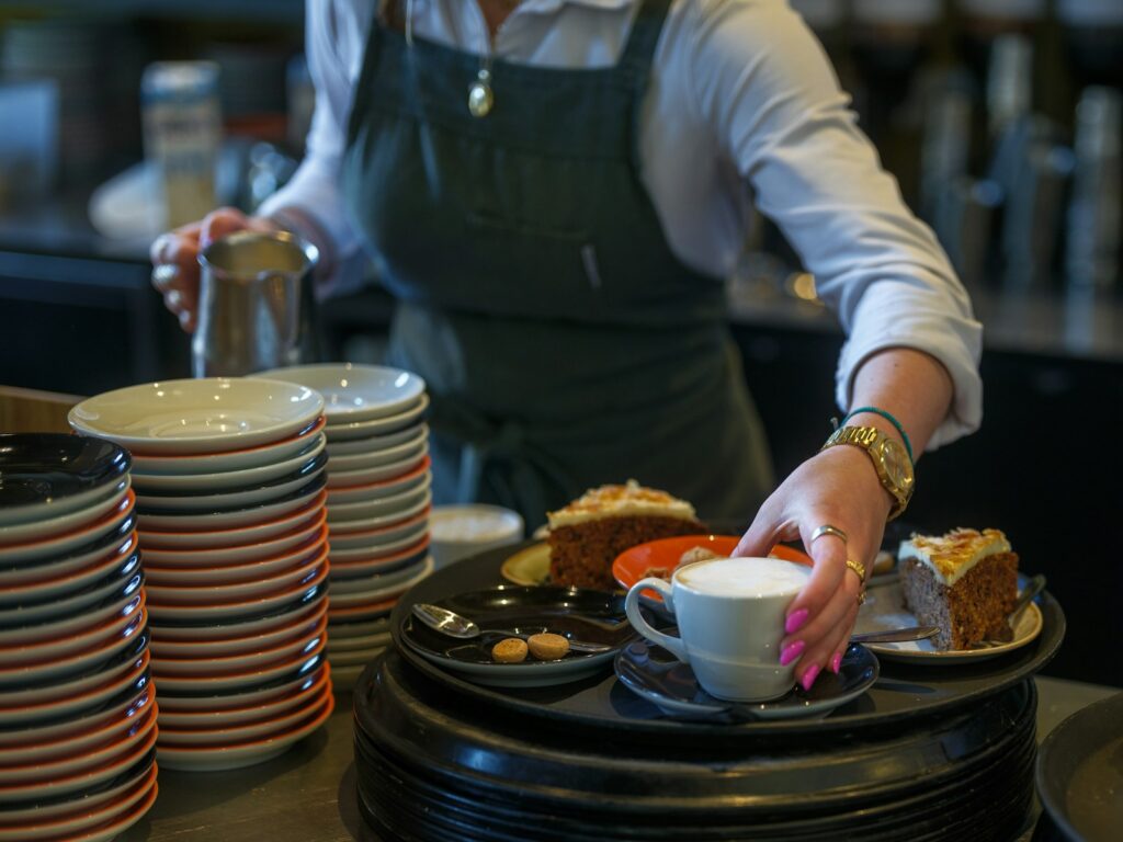 Una mesera atiende la mesa de un restaurante, decorada con platos y copas para los comensales